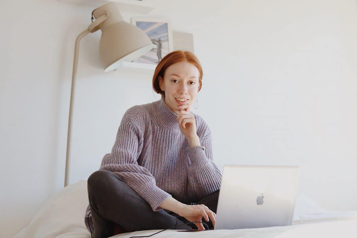 woman in gray sweater sitting on chair using macbook