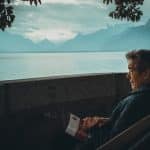 man sitting while holding a book watching on body of water