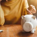 woman hand putting money coin into piggy for saving money wealth and financial concept.